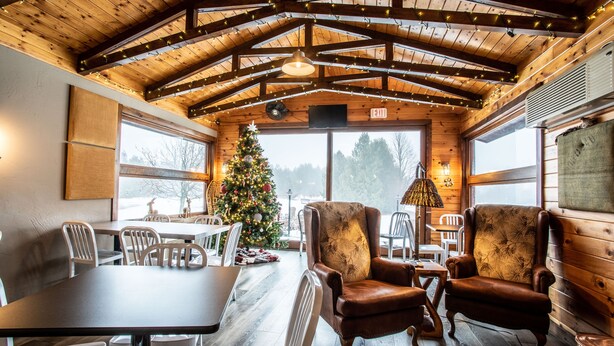 Un interior acogedor con vigas de madera, un árbol de Navidad, sillones de cuero y un amplio ventanal con vistas.