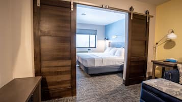 A hotel room with a sliding door leading to a bedroom, a desk with a lamp, and a patterned carpet.