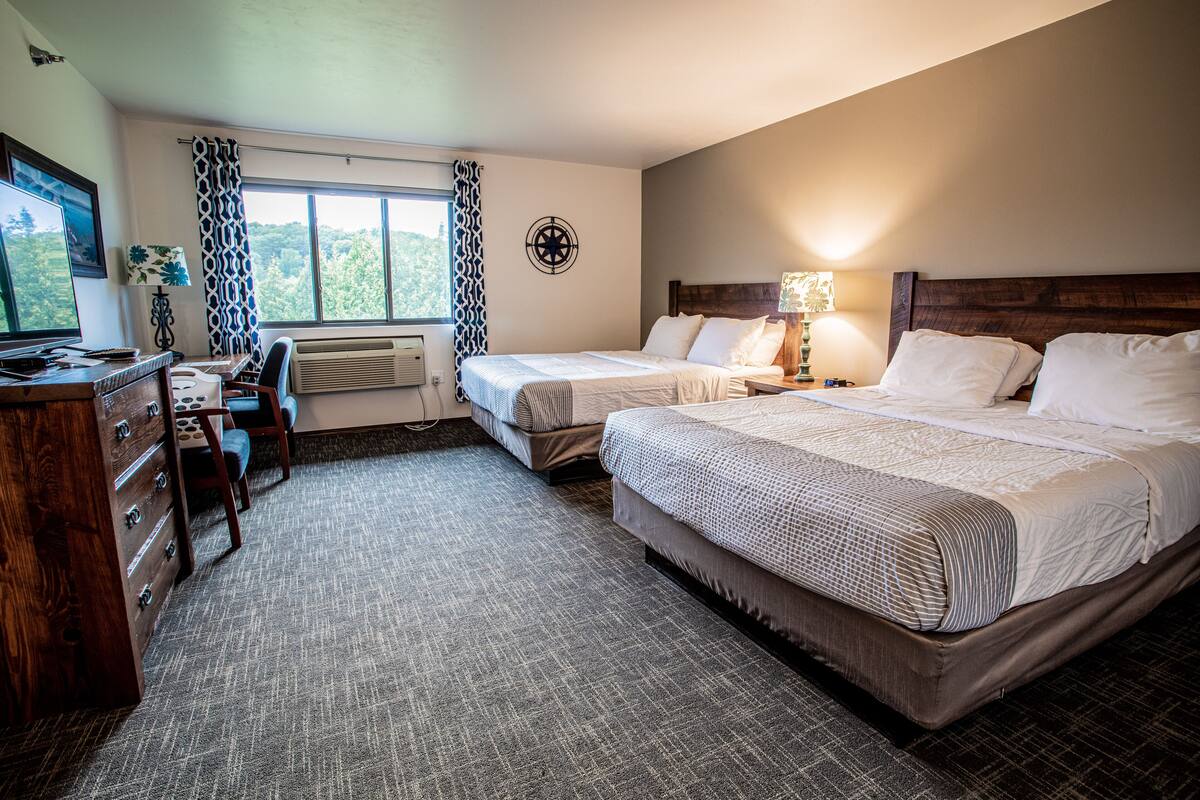 A hotel room with two beds, a desk with a computer, a chair, and a window with curtains.