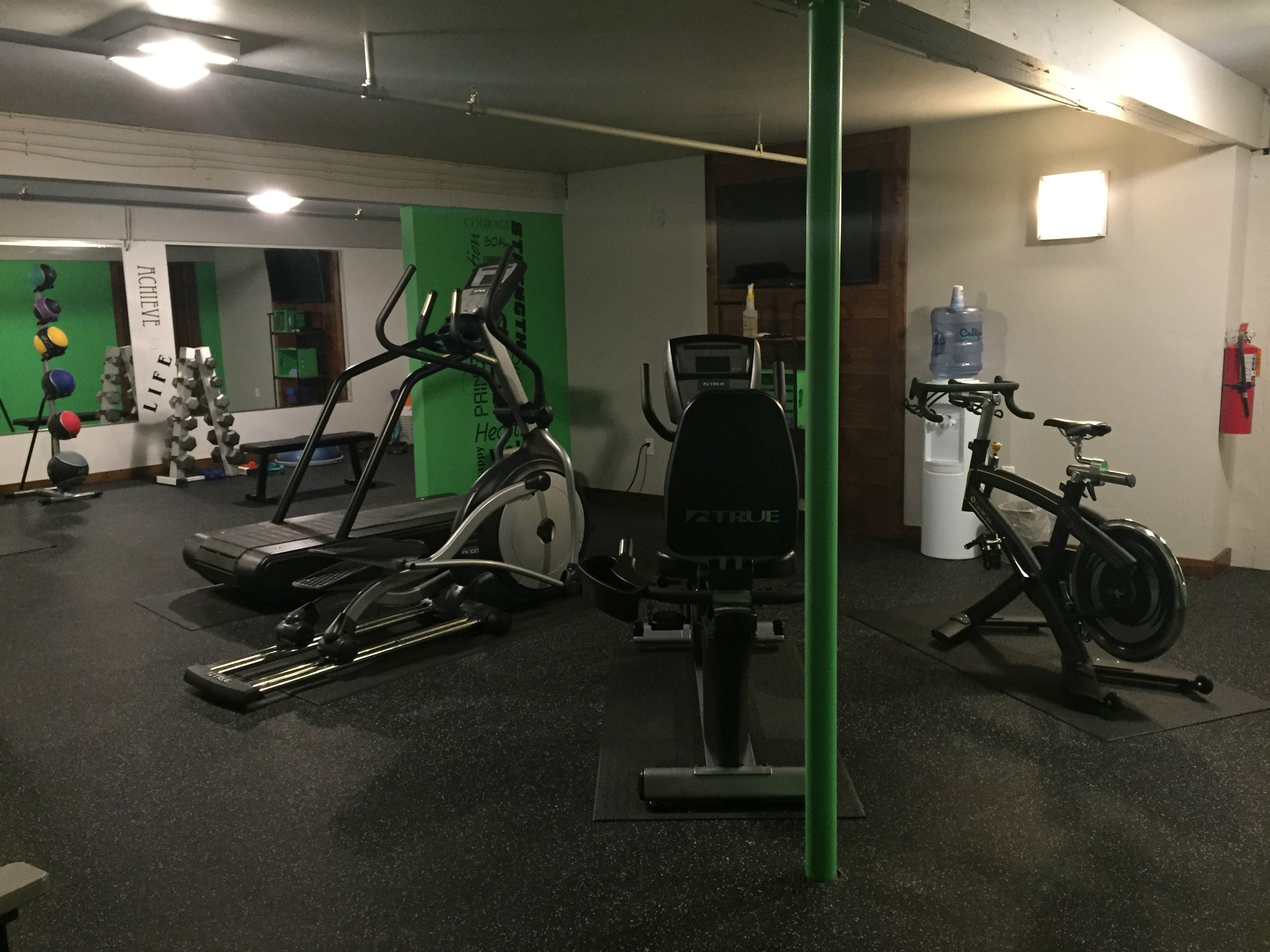 Un gimnasio con equipo de ejercicio, dispensador de agua y extintor.