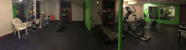 Un gimnasio con equipo de ejercicio, un espejo y una pared verde.