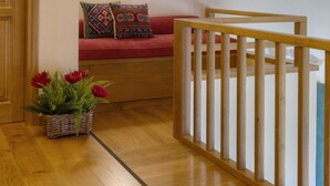 A wooden-floored room with a red sofa, a wooden railing, and a small plant. - Ritsos Guesthouse (Monemvasia)