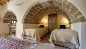 A room with two beds, a wooden chair, a patterned rug, and stone arches. - Ritsos Guesthouse (Monemvasia)