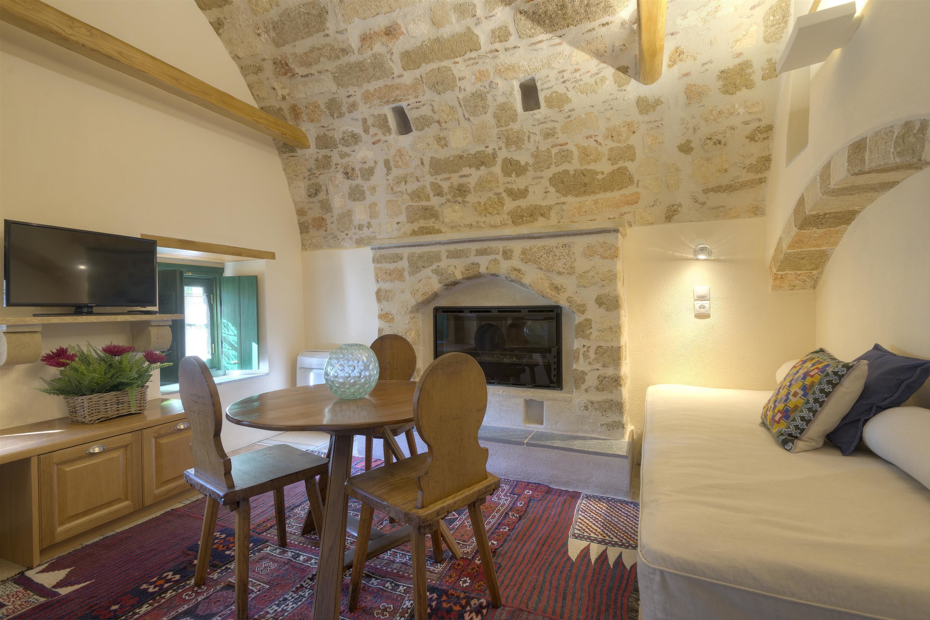 Una habitación acogedora con techo de piedra, chimenea, comedor con mesa y sillas, y sofá con cojines.