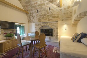 Una habitación acogedora con techo de piedra, chimenea, comedor con mesa y sillas, y sofá con cojines.