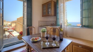 A dining area with a table set for two, a bottle of wine, and a plate of food. - Ritsos Guesthouse (Monemvasia)
