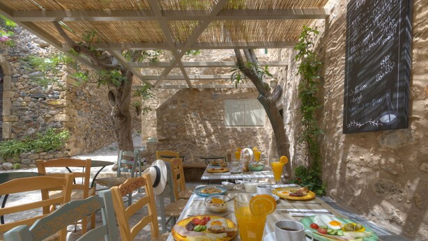 An outdoor dining area with stone walls, wooden furniture, and a menu board. - Ritsos Guesthouse (Monemvasia)