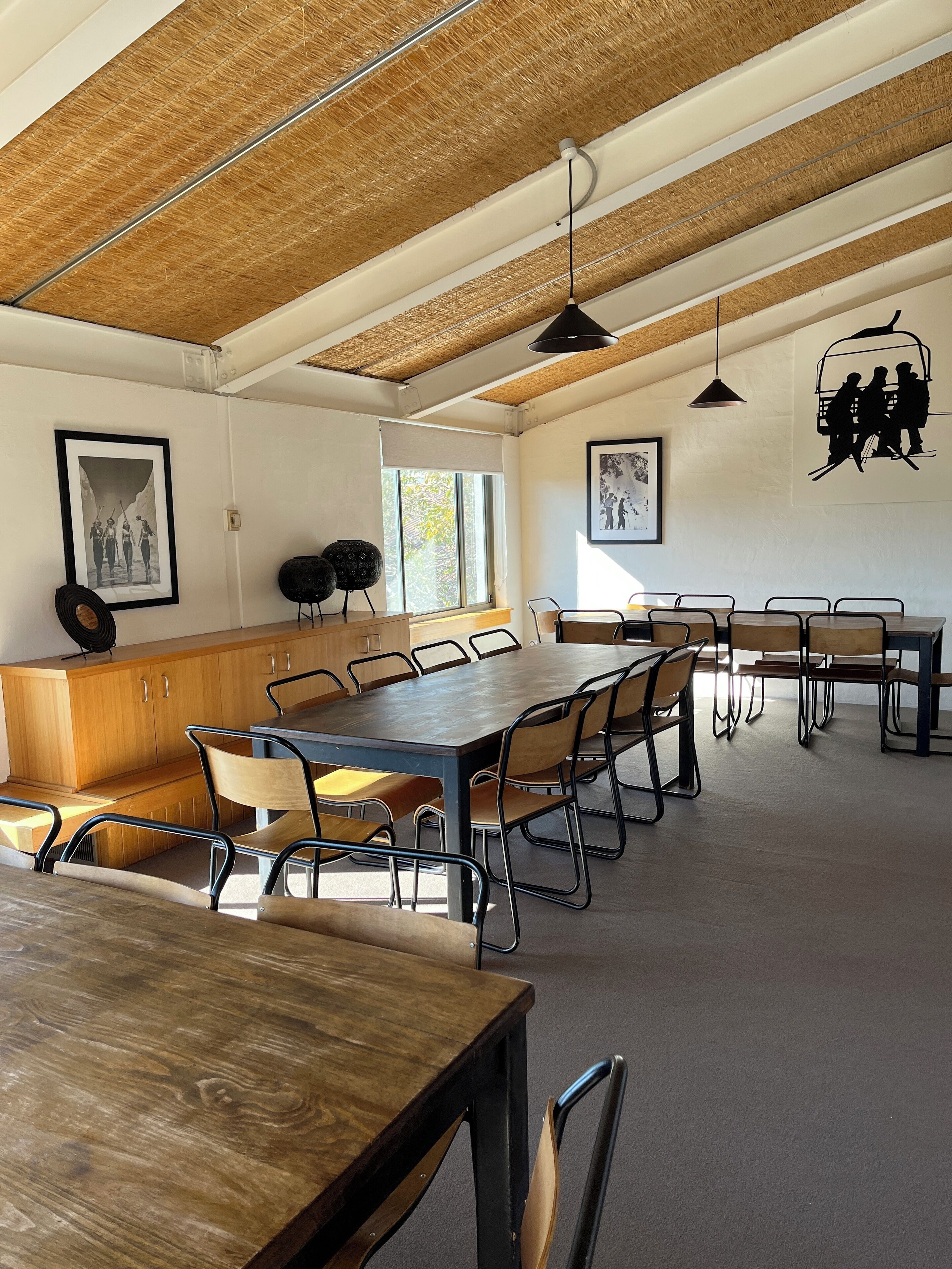 Une salle de réunion spacieuse, dotée d’une grande table en bois, de nombreuses chaises et d’un plafond haut avec des poutres apparentes.