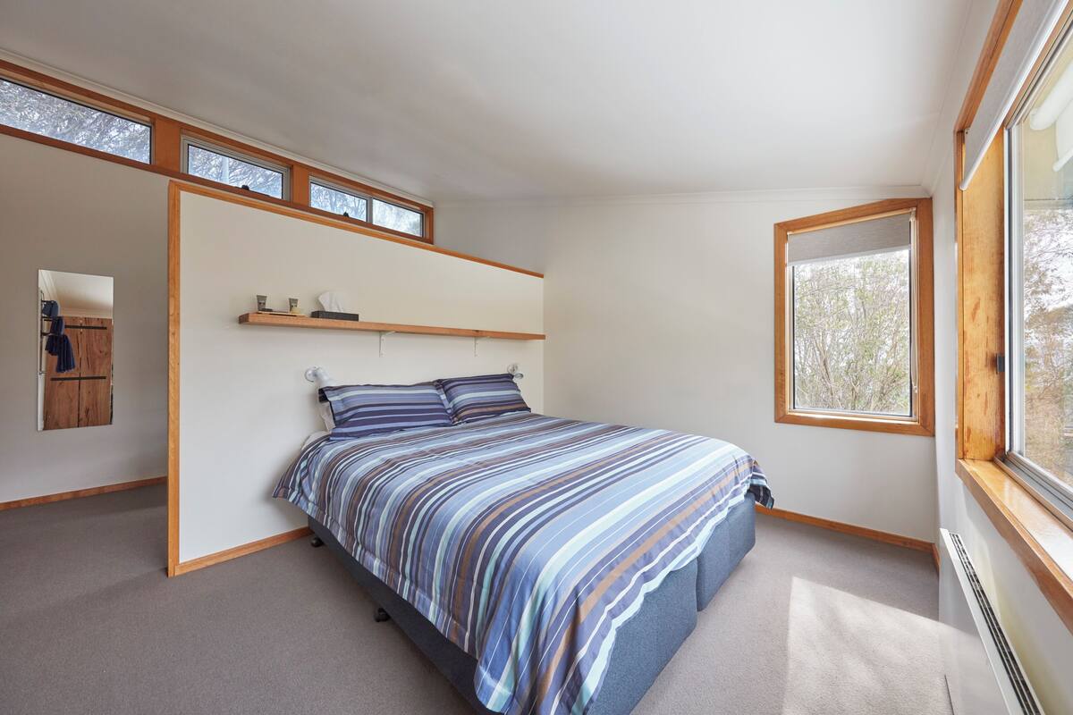 A bedroom with a bed, a shelf above the bed, a window, and a radiator.