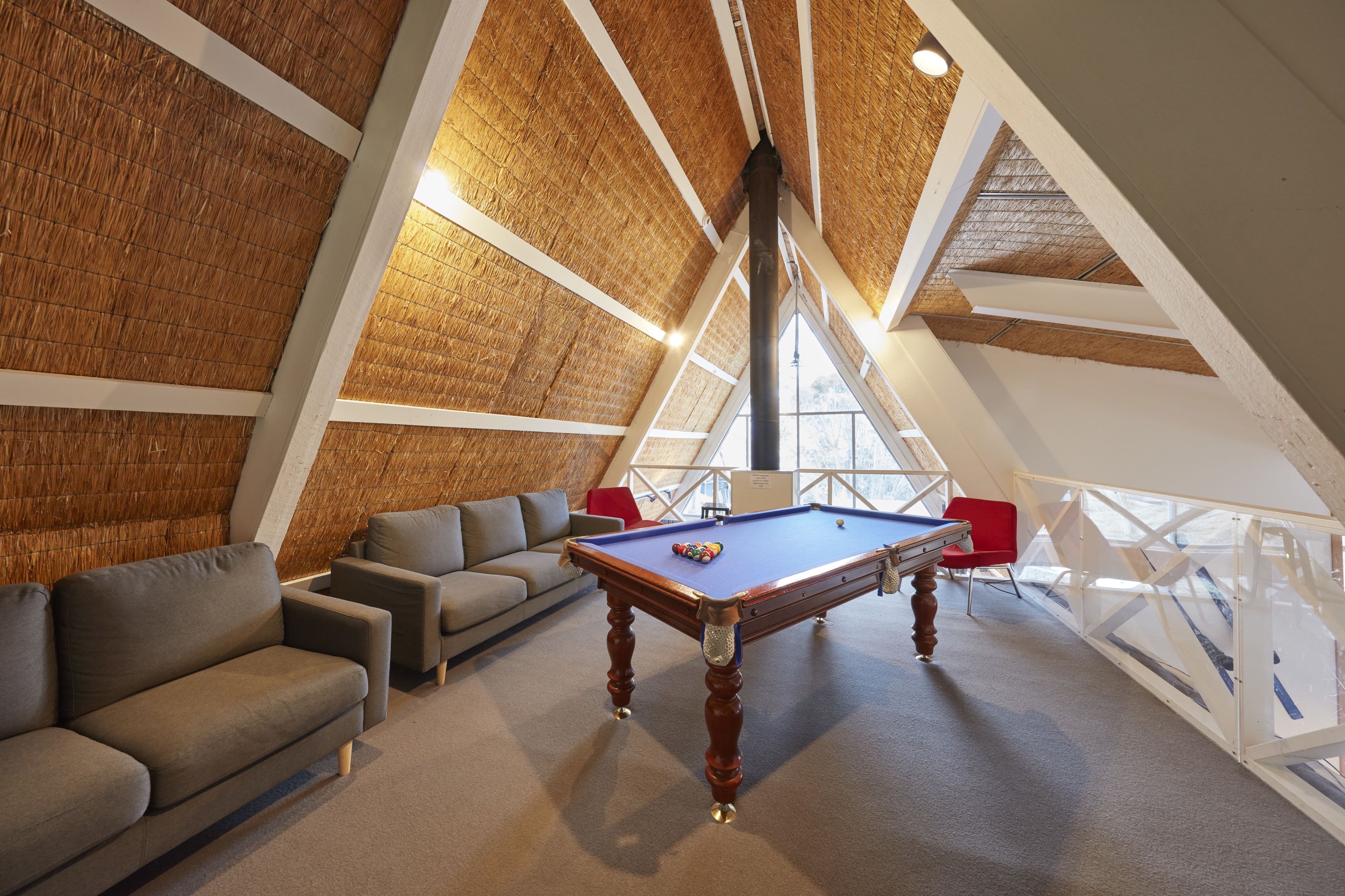 A cozy loft-style room with a pool table, comfortable seating, and a high ceiling with exposed beams.