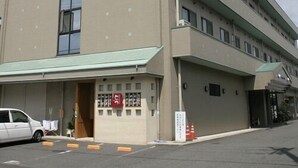 A multi-story building with a flat facade, large windows on the ground floor, and a parking area with a white car. - Toyooka Park Hotel (Toyooka)