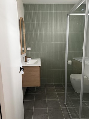 Un baño moderno con cabina de ducha, inodoro y tocador con espejo.
