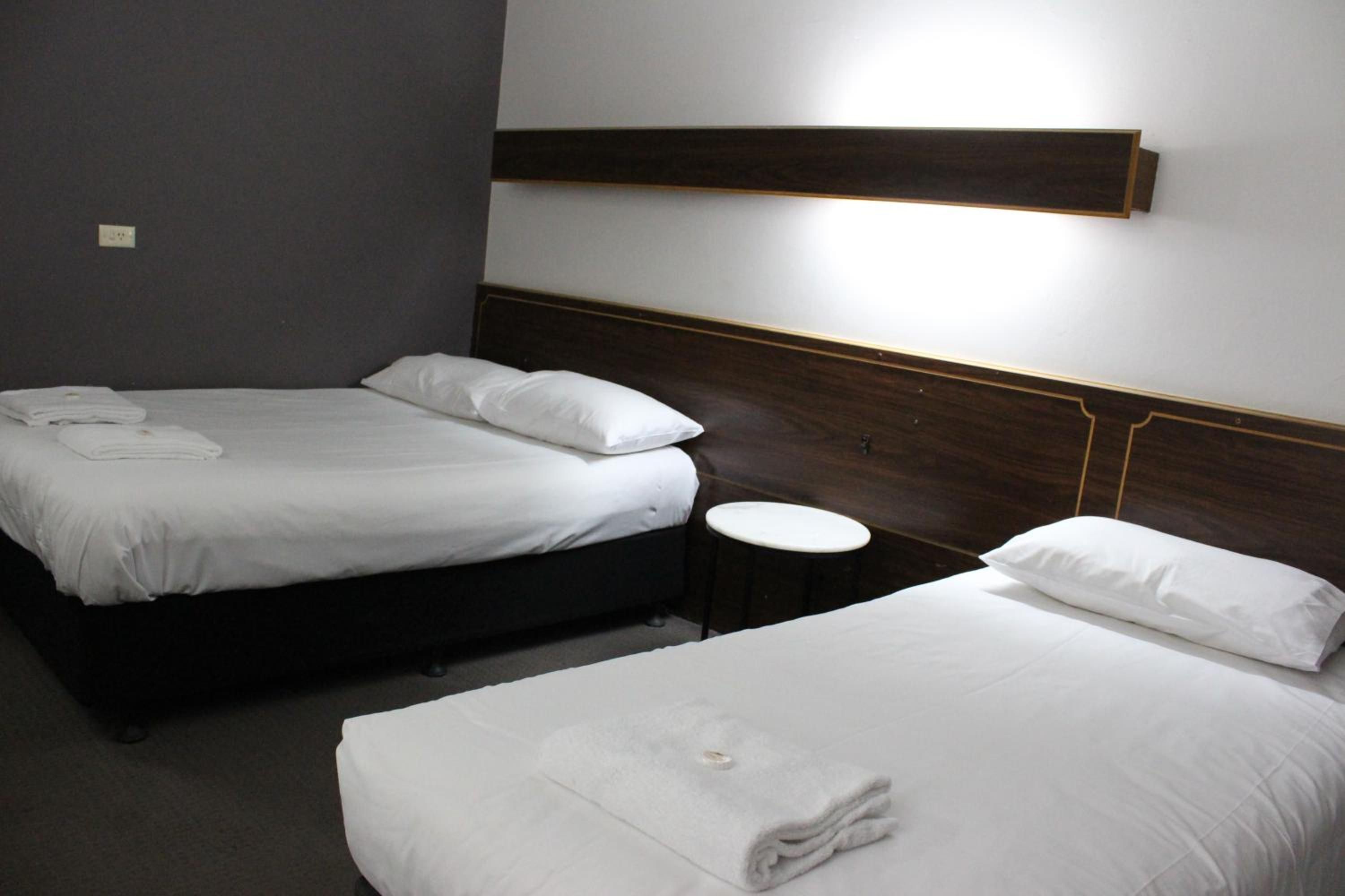 Une chambre d’hôtel avec deux lits, chacun doté de draps et d’oreillers blancs, une petite table ronde et un luminaire fixé au mur.