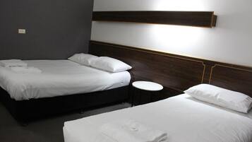 A hotel room with two beds, each with white linens and pillows, a small round table, and a wall-mounted light fixture.