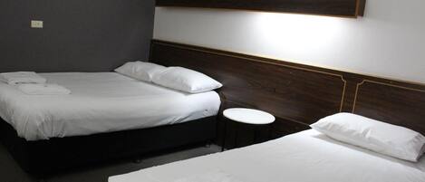 Une chambre d’hôtel avec deux lits, chacun doté de draps et d’oreillers blancs, une petite table ronde et un luminaire fixé au mur.