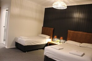 Habitación de hotel con dos camas, cabecero de madera oscura, techo blanco y lámpara colgante.