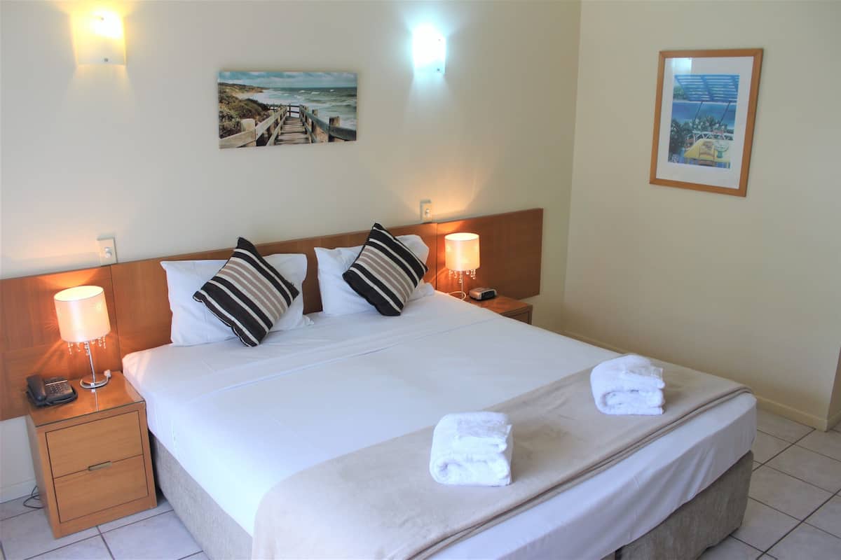 A neatly made bed with white linens, two pillows, a bedside lamp, and a folded towel on the bed.