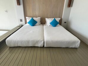A double bed with white linens and two blue pillows, a wooden headboard, and a wooden floor. - Bari Lamai Resort (Rayong)