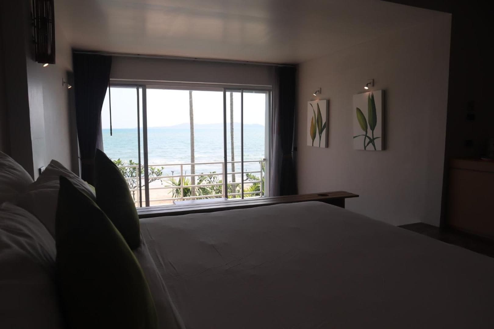 A bedroom with a large bed, a view of the sea, and two wall-mounted plant paintings.