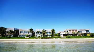 Un hotel frente a la playa con edificios de varios pisos, palmeras y una vista despejada del océano.