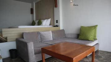A modern living room with a grey sofa, a wooden coffee table, and a small bed with a wooden headboard.