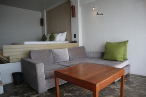 A modern living room with a grey sofa, a wooden coffee table, and a small bed with a wooden headboard. - Bari Lamai Resort (Rayong)