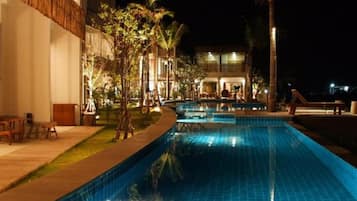 A swimming pool with a tiled edge, surrounded by a landscaped area with trees and a building in the background.
