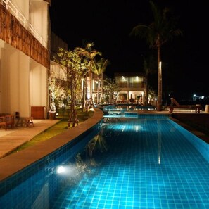 A swimming pool with a tiled edge, surrounded by a landscaped area with trees and a building in the background. - Bari Lamai Resort (Rayong)