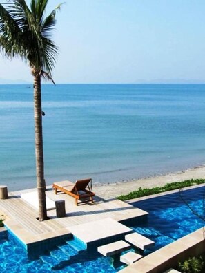 Un área junto a la piscina con una tumbona, una palmera y vista al mar.