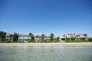 Ett hotell vid stranden med flera byggnader, kristallklart vatten och palmer.