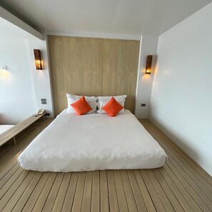 A large bed with white bedding and two orange pillows, a wooden floor, and two wall-mounted light fixtures. - Bari Lamai Resort (Rayong)