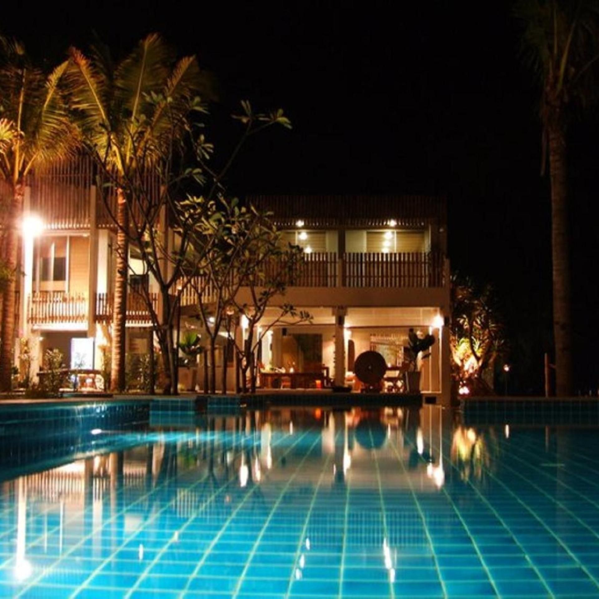 A nighttime view of a hotel with a swimming pool, palm trees, and a lit building facade.