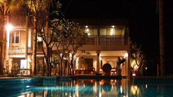 A nighttime view of a hotel with a swimming pool, palm trees, and a lit building facade.