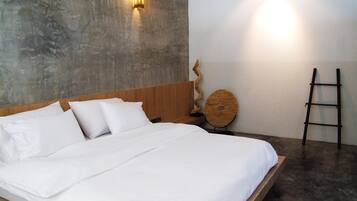 A bedroom with a large bed, a wooden headboard, a concrete wall, a round wooden object, and a black ladder.