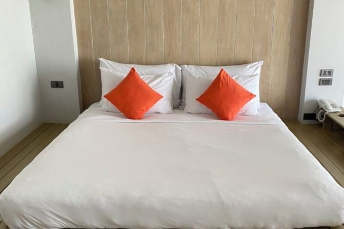 A hotel room with a wooden headboard, white bedding, and two orange pillows.