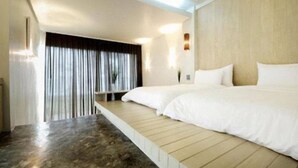 Habitación de hotel con una cama grande, un banco de madera y vistas a través de una ventana con cortinas.