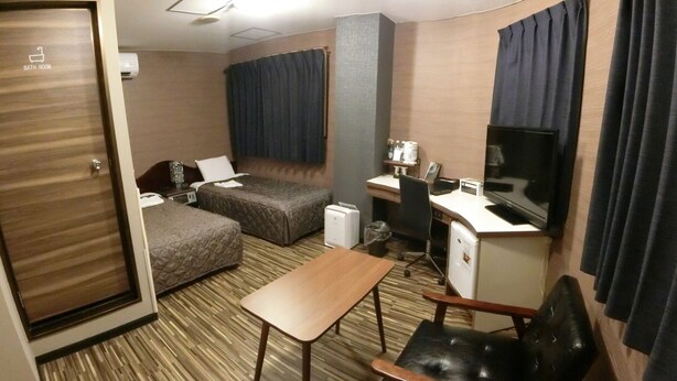 Una habitación de hotel con cama, escritorio, silla, televisor y puerta del baño.