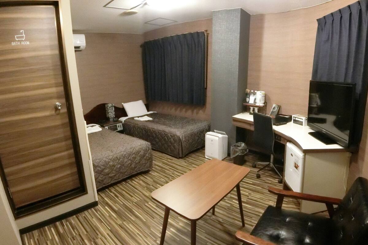 A hotel room with a bed, a desk, a chair, a TV, and a bathroom door.