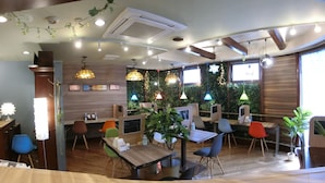Interior de un restaurante con mesas de madera, sillas coloridas, lámparas colgantes y una pared verde con plantas.