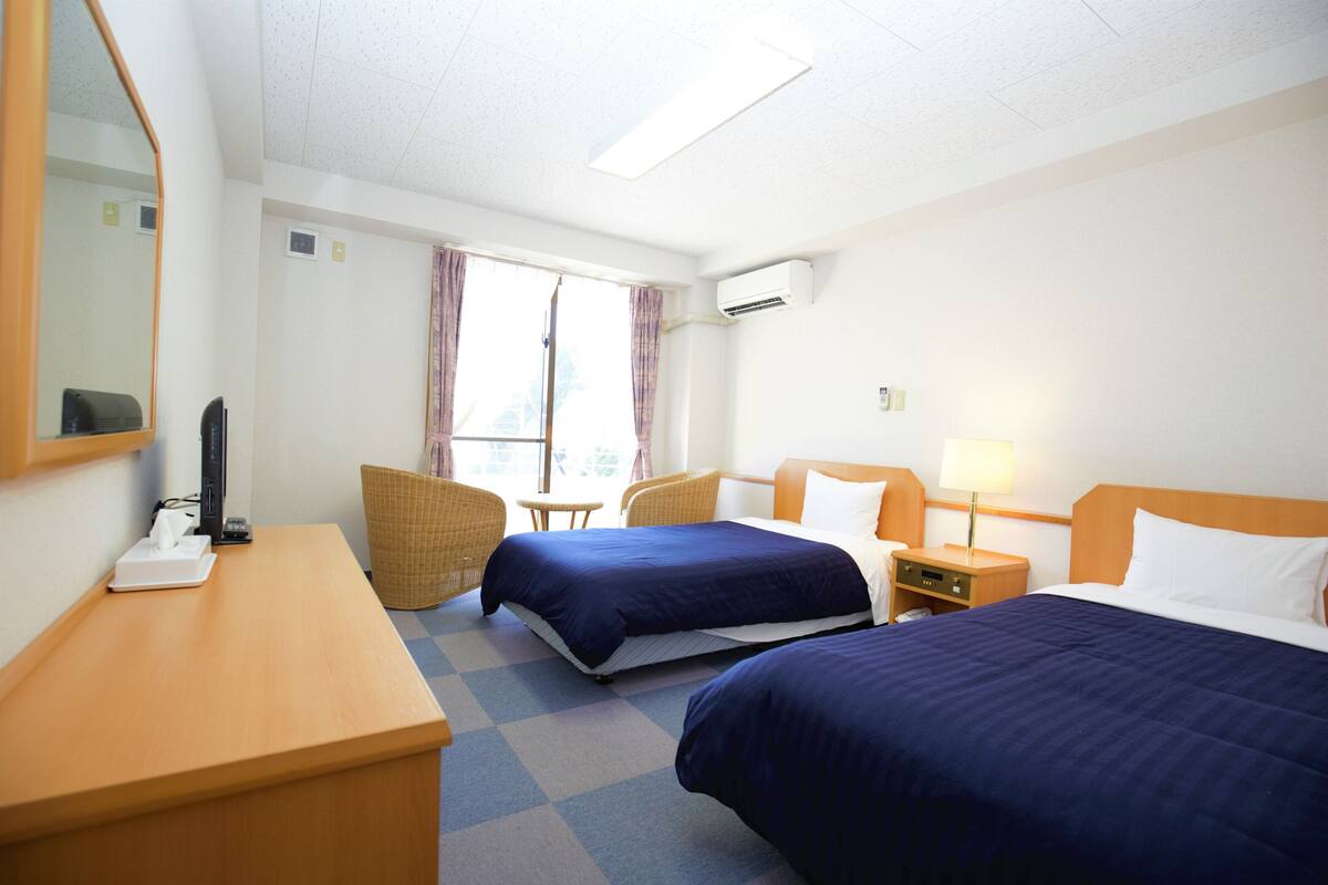 Habitación de hotel con dos camas, un escritorio, una silla y una ventana con cortinas.