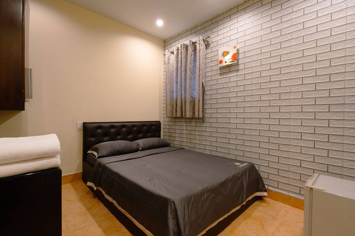 Un dormitorio con cama, una mesita de noche, una lámpara de pared y una pared con diseño de ladrillos.