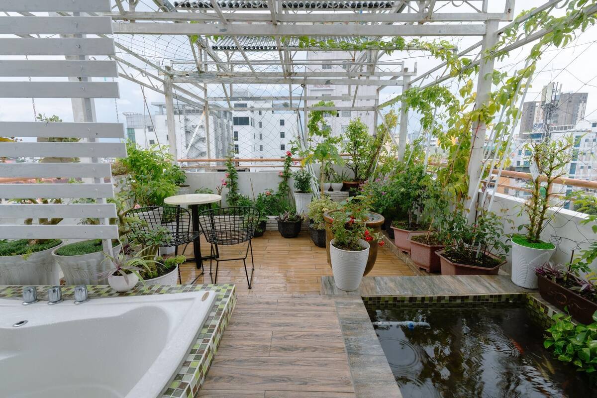 Un jardín en la azotea con diversos maceteros, una pequeña piscina y un área de estar con mesa y sillas.
