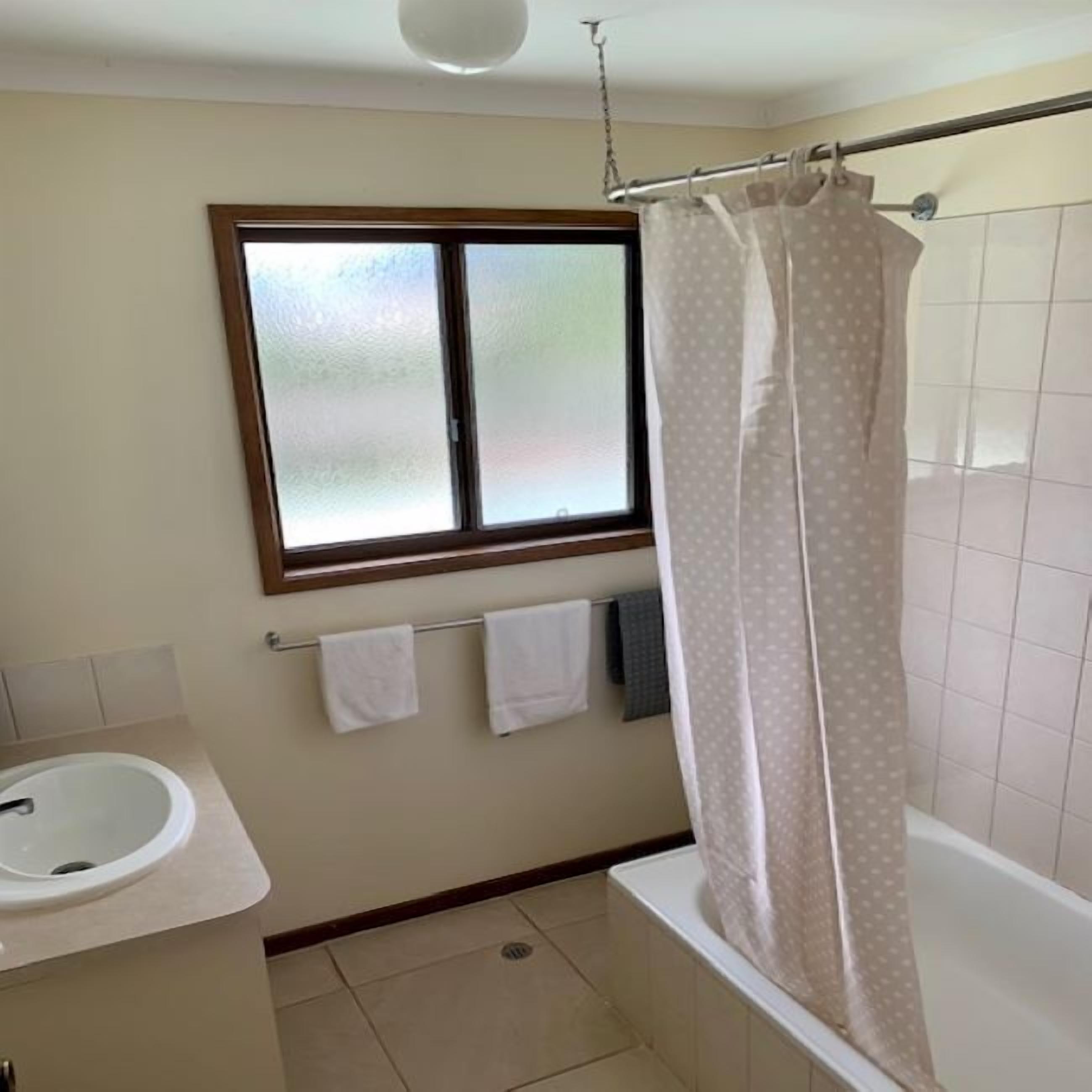 A bathroom with a window, a shower curtain, a sink, and a towel rack.