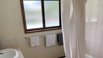 Ein Badezimmer mit Fenster, Duschvorhang, Waschbecken und Handtuchhalter.