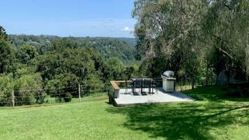 A grassy outdoor area with a barbecue setup and a view of a forested hill.