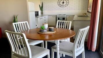 Un coin repas avec une table ronde en bois entourée de chaises blanches. Une horloge est fixée au mur au-dessus de la table.