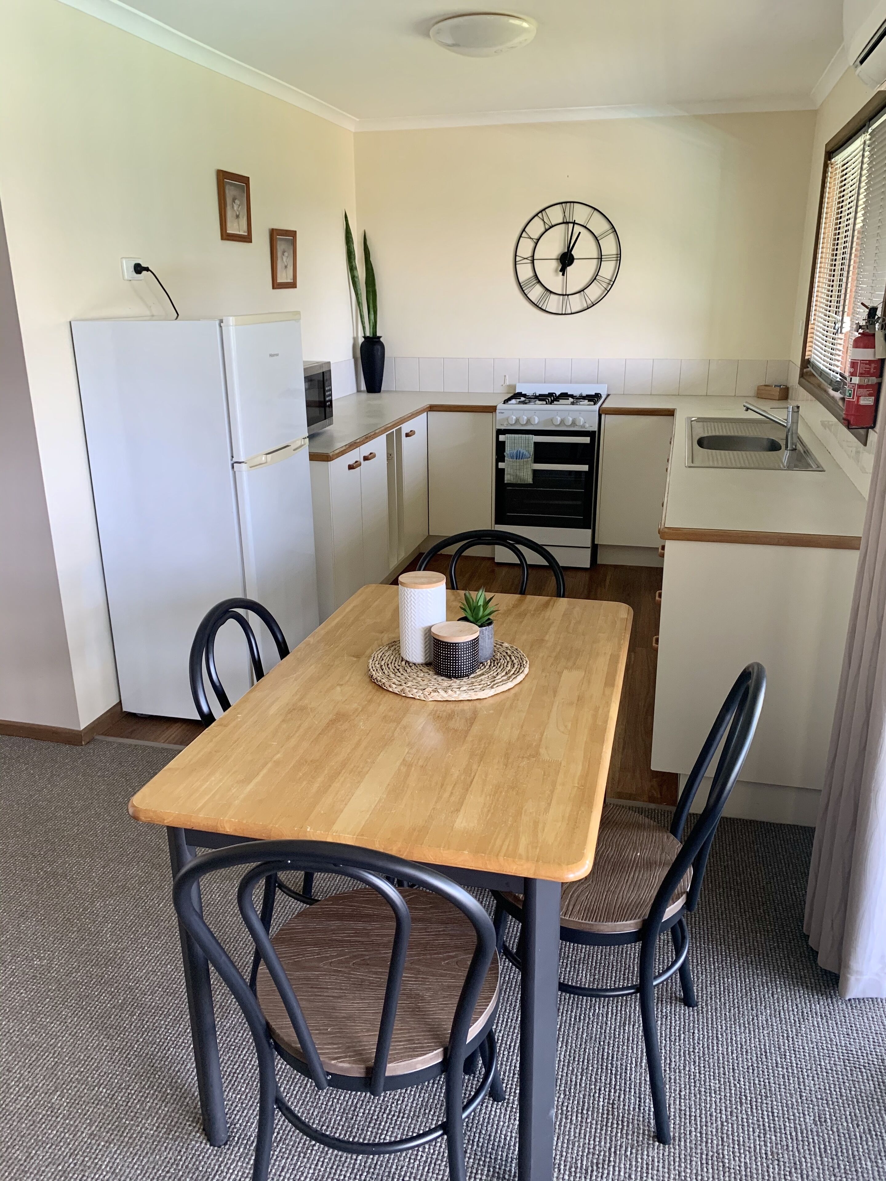 A compact kitchen with a wooden table, chairs, a clock, a refrigerator, and a stove.
