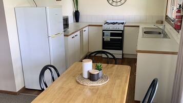 Een kleine keuken met een houten tafel, stoelen, een klok, een koelkast en een fornuis.
