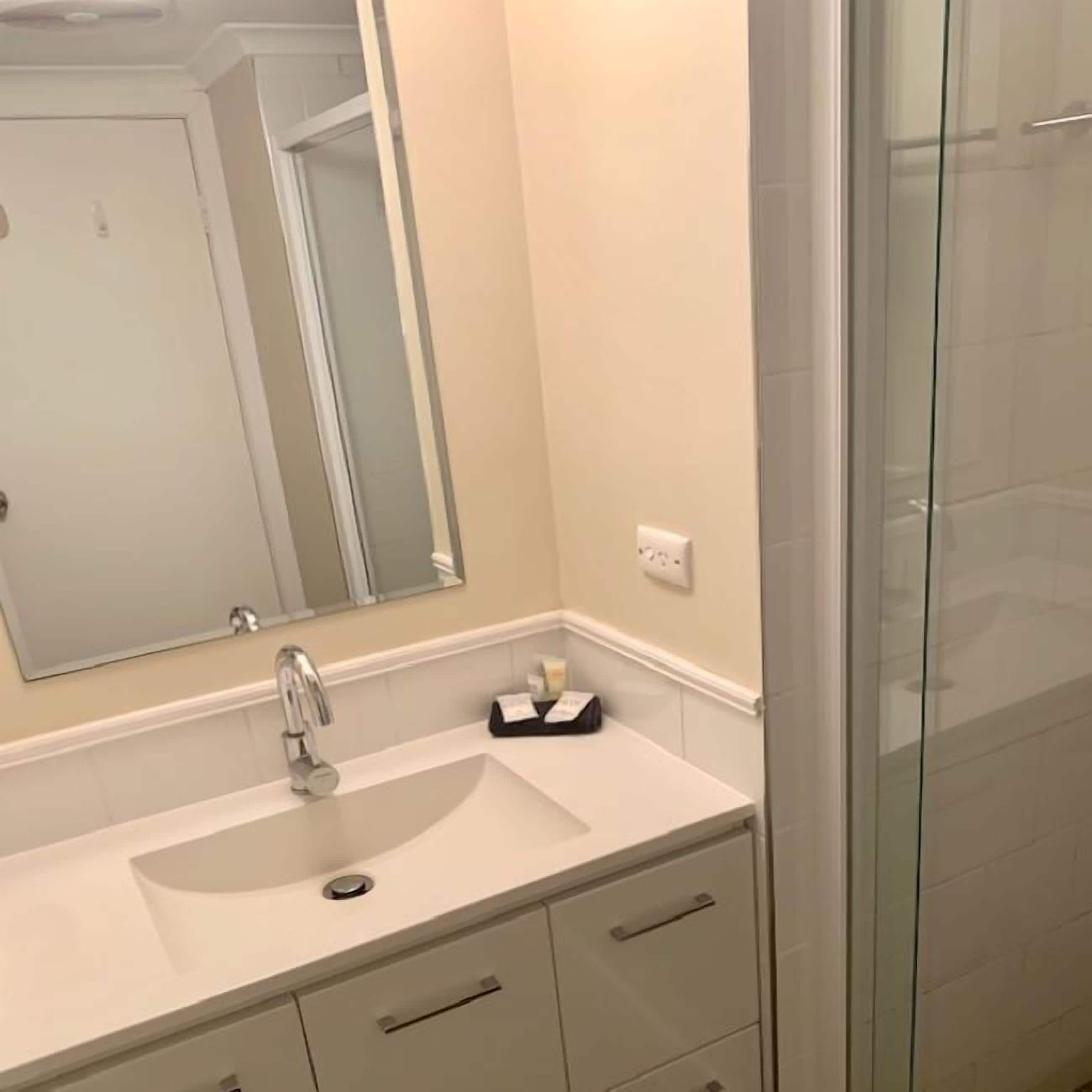 A bathroom with a white sink, a mirror, and a glass shower enclosure.
