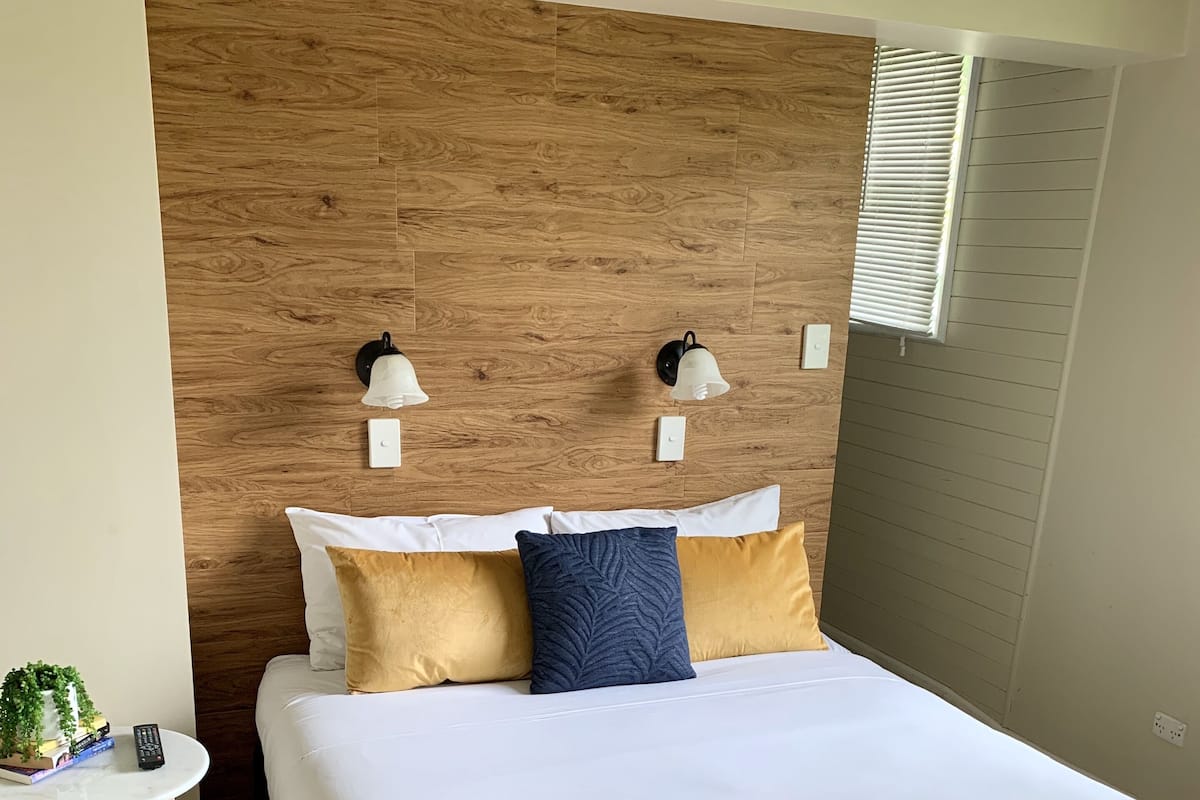 A neatly made bed with white and gold bedding, a wooden headboard, and two wall-mounted light fixtures.